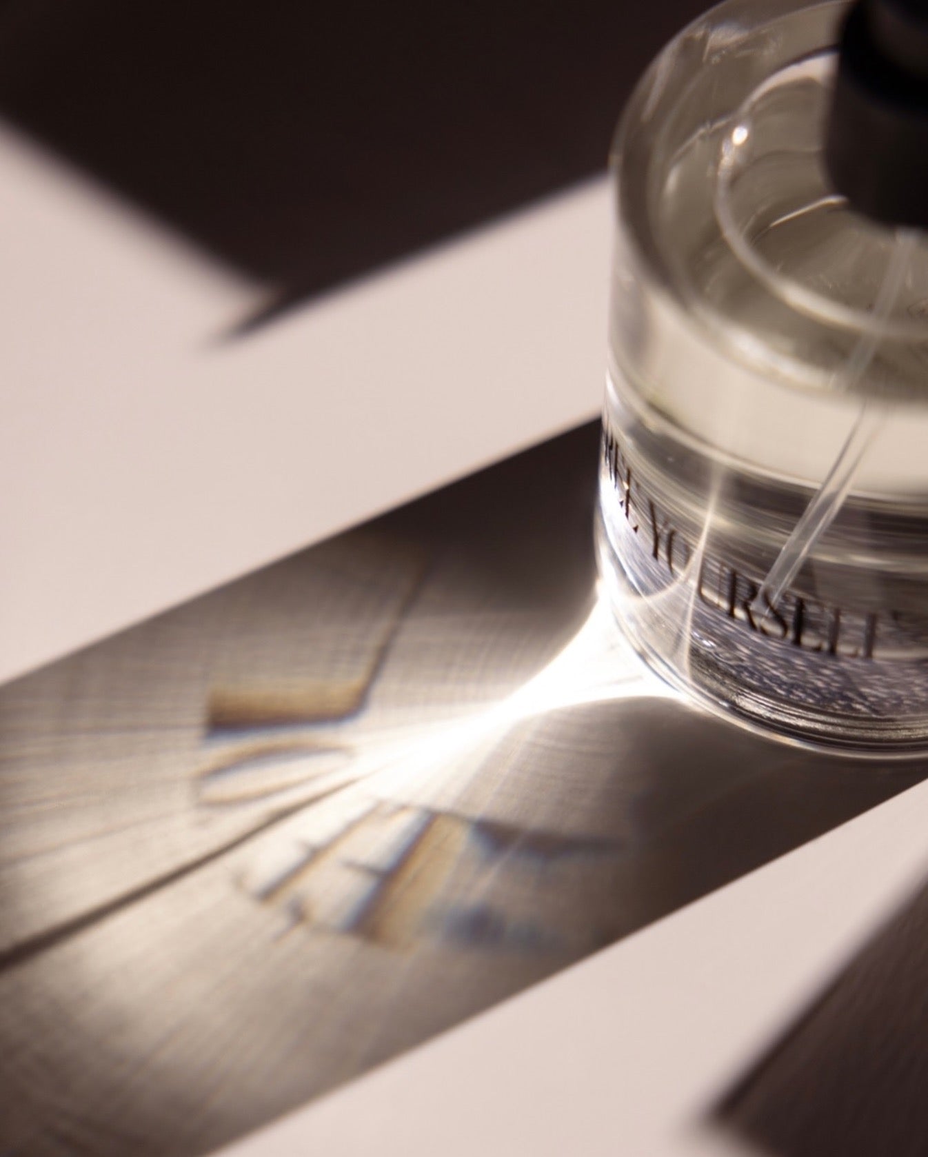 Perfume bottle casting a shadow on a white surface.