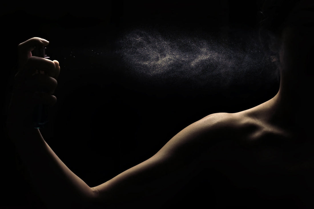 Side view of someone backlit on a black background spraying the best perfumes on their neck.